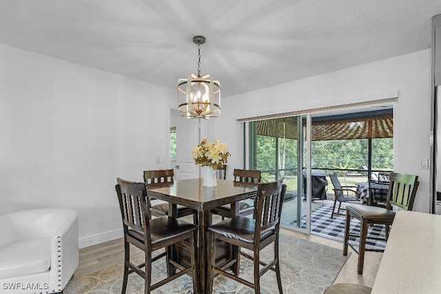 dining space with baseboards, a textured ceiling, light wood-style flooring, and an inviting chandelier