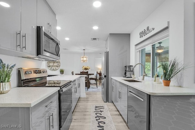 kitchen featuring stainless steel appliances, a sink, visible vents, gray cabinets, and decorative light fixtures