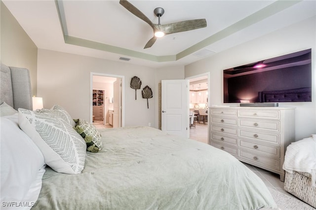 bedroom featuring visible vents, a raised ceiling, a ceiling fan, ensuite bath, and light tile patterned flooring