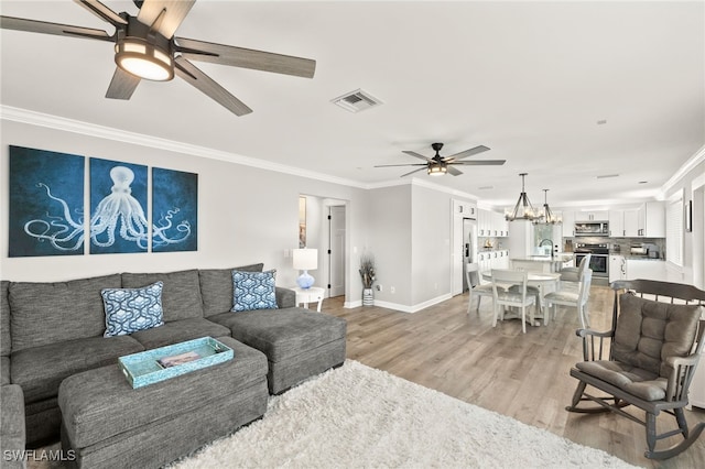 living room featuring visible vents, ceiling fan with notable chandelier, light wood-style floors, and ornamental molding