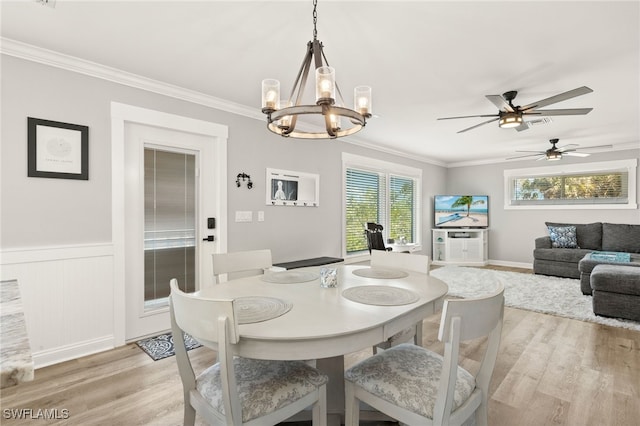 dining room with crown molding, light wood-style flooring, ceiling fan with notable chandelier, and wainscoting