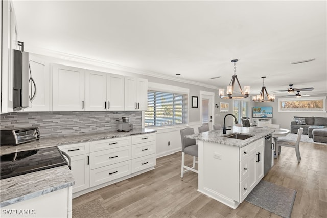 kitchen with a sink, open floor plan, a toaster, crown molding, and light wood finished floors