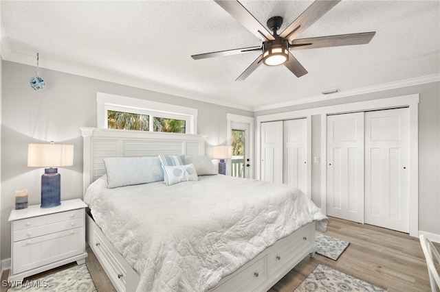 bedroom featuring a ceiling fan, ornamental molding, multiple closets, a textured ceiling, and light wood-type flooring