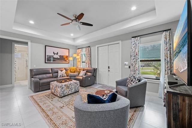 living room featuring light tile patterned floors, baseboards, and a tray ceiling