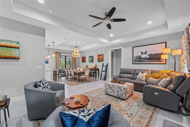 living area with baseboards, ceiling fan with notable chandelier, a tray ceiling, and recessed lighting