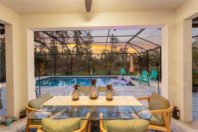 pool at dusk with a lanai, ceiling fan, an outdoor pool, and a patio