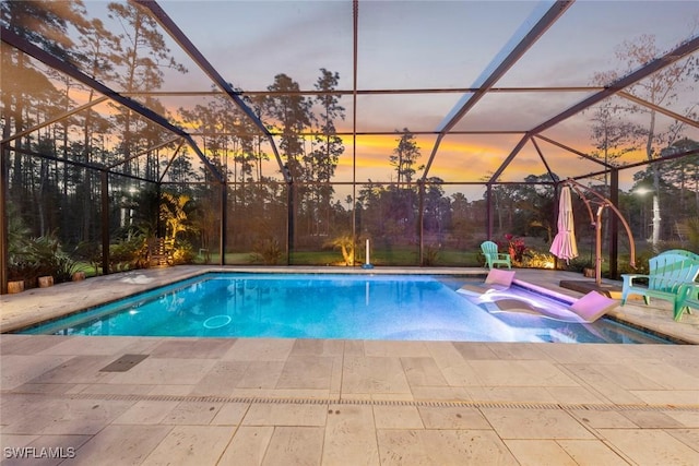 pool at dusk featuring glass enclosure, a hot tub, a patio area, and an outdoor pool