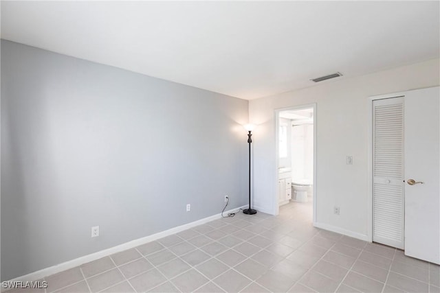 unfurnished bedroom with ensuite bath, visible vents, light tile patterned floors, and baseboards