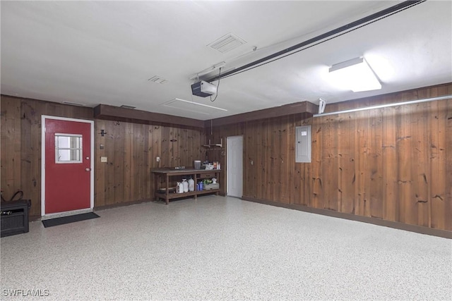 garage featuring a garage door opener, electric panel, wood walls, and visible vents