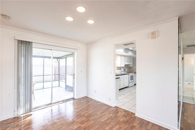 spare room with light wood-style floors, baseboards, visible vents, and crown molding