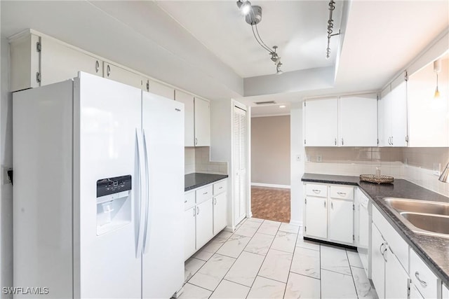 kitchen featuring white refrigerator with ice dispenser, marble finish floor, decorative backsplash, dark countertops, and a raised ceiling