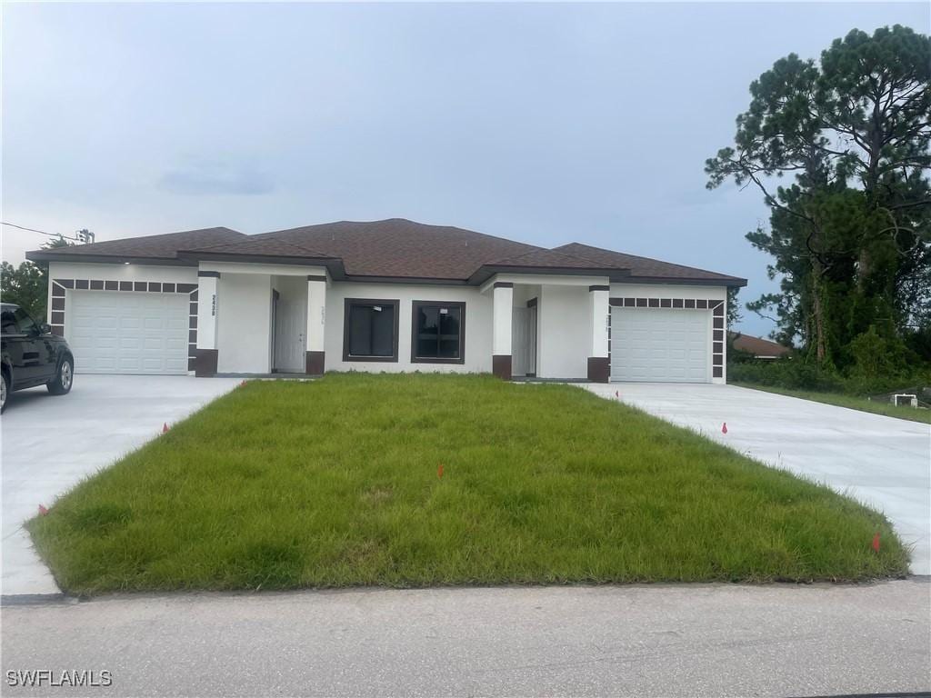 prairie-style house with a garage, driveway, a front lawn, and stucco siding