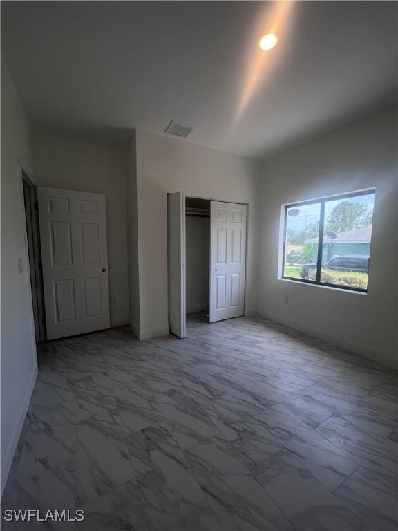 unfurnished bedroom featuring marble finish floor, visible vents, baseboards, and a closet