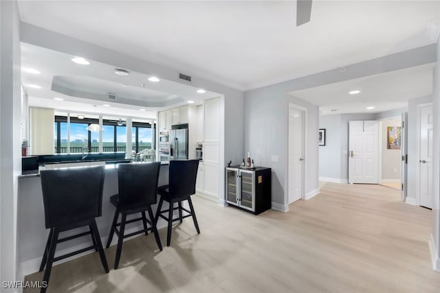 kitchen featuring light wood finished floors, a raised ceiling, white cabinets, stainless steel fridge, and a kitchen bar