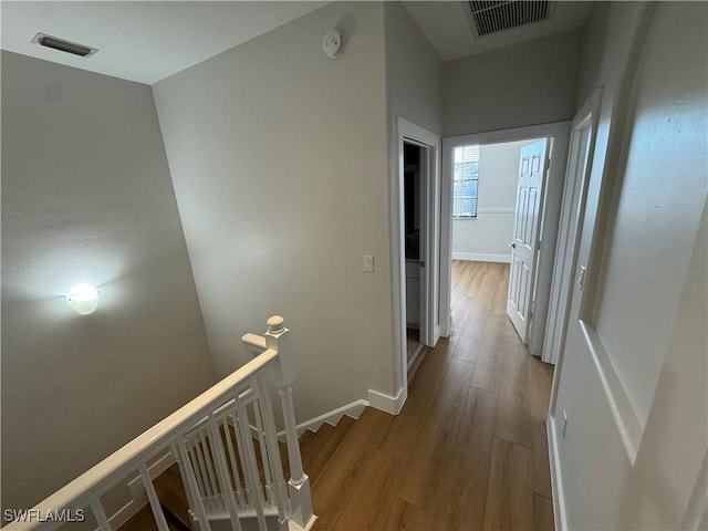 corridor with an upstairs landing, wood finished floors, visible vents, and baseboards