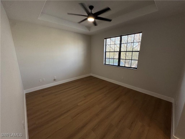 unfurnished room featuring a ceiling fan, a raised ceiling, dark wood finished floors, and baseboards