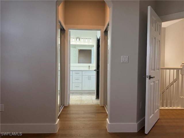 hallway with an upstairs landing, light wood-type flooring, a sink, and baseboards