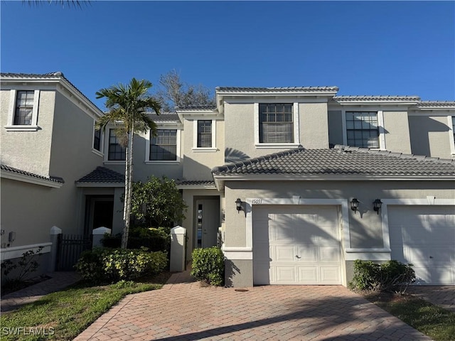 townhome / multi-family property with driveway, an attached garage, a tiled roof, and stucco siding