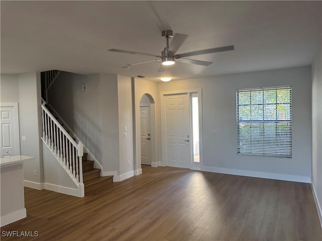 entrance foyer featuring baseboards, arched walkways, ceiling fan, dark wood-type flooring, and stairs