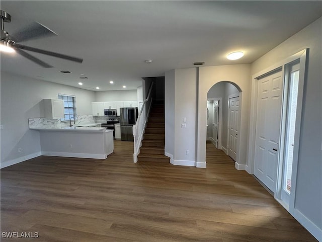 kitchen featuring arched walkways, appliances with stainless steel finishes, a peninsula, light countertops, and white cabinetry