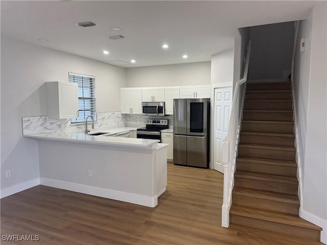 kitchen with a peninsula, a sink, white cabinetry, light countertops, and appliances with stainless steel finishes