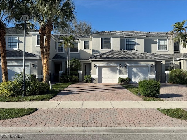 view of property with a garage, a tiled roof, decorative driveway, and stucco siding