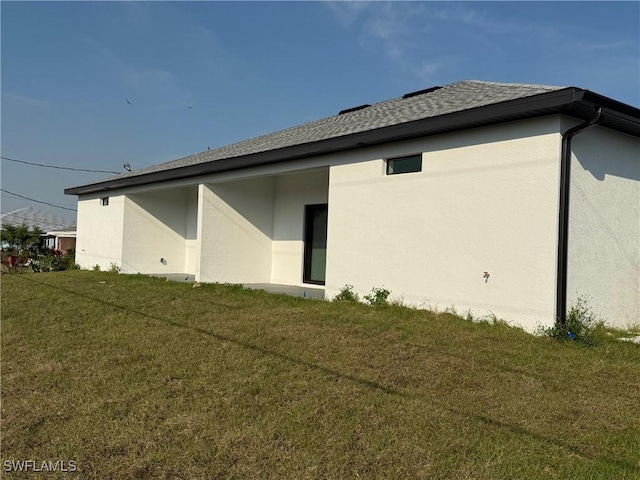 back of house with a yard, roof with shingles, and stucco siding