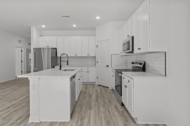 kitchen with white cabinets, appliances with stainless steel finishes, a kitchen island with sink, light countertops, and a sink