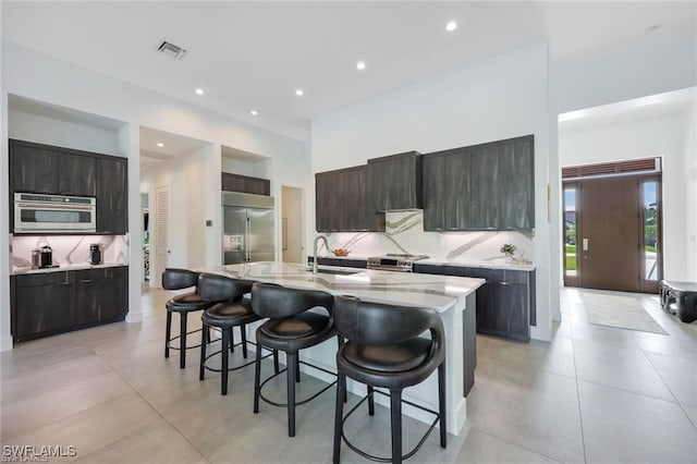 kitchen featuring dark brown cabinetry, tasteful backsplash, an island with sink, a breakfast bar, and stainless steel appliances