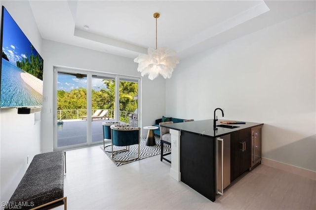 kitchen with baseboards, hanging light fixtures, a tray ceiling, dark brown cabinets, and a sink