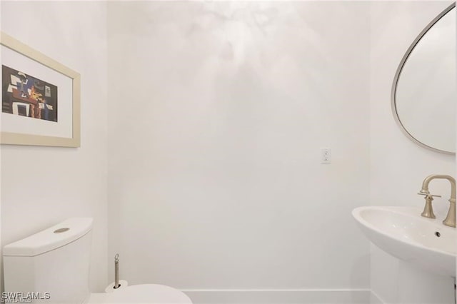 half bath featuring toilet, baseboards, and a sink