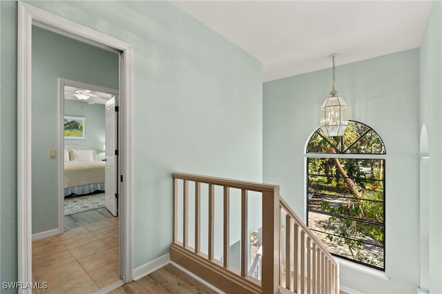 corridor featuring a chandelier, baseboards, light wood-style flooring, and an upstairs landing