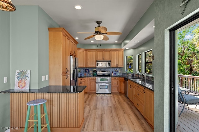 kitchen featuring appliances with stainless steel finishes, light wood-style flooring, a peninsula, and decorative backsplash