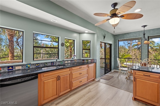 kitchen with light wood-style flooring, dark stone counters, a sink, dishwasher, and pendant lighting