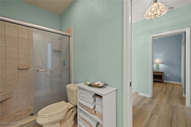 full bath with a notable chandelier, toilet, a stall shower, wood finished floors, and baseboards