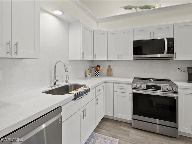 kitchen with stainless steel appliances, a sink, white cabinetry, light wood-style floors, and decorative backsplash