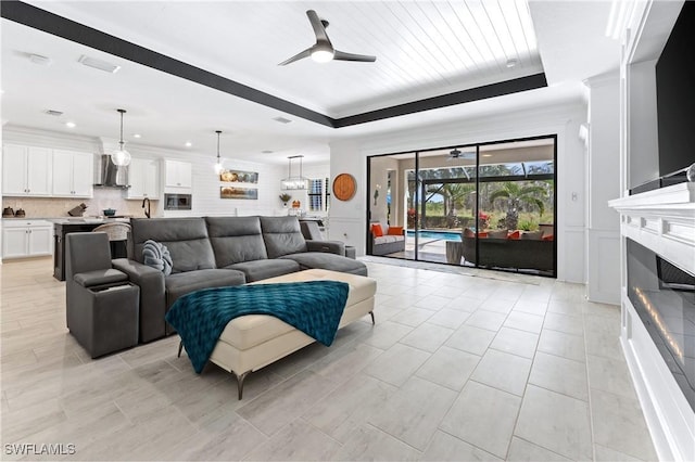 living area featuring visible vents, a ceiling fan, a lit fireplace, a tray ceiling, and crown molding