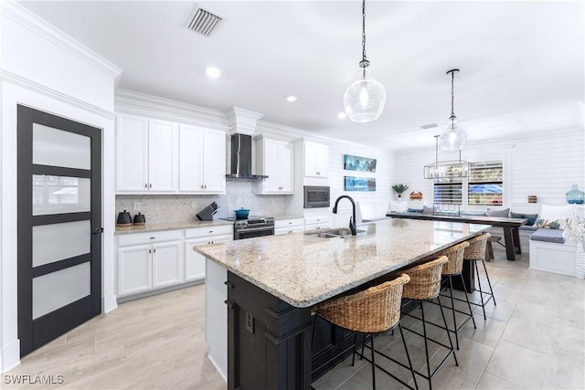 kitchen featuring visible vents, white cabinets, wall chimney exhaust hood, a kitchen island with sink, and a sink