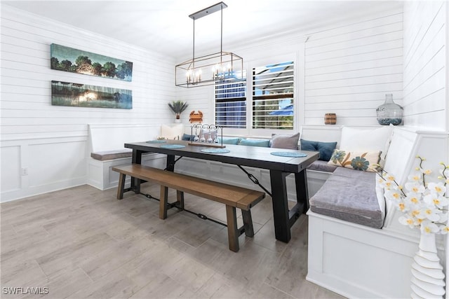 dining space with breakfast area, a decorative wall, an inviting chandelier, ornamental molding, and light wood-type flooring