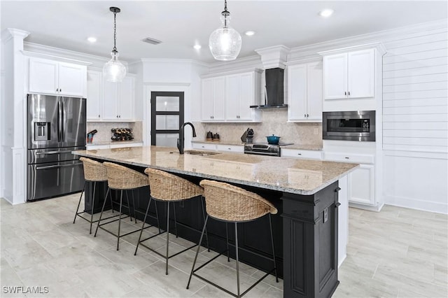 kitchen featuring stainless steel appliances, white cabinets, a kitchen island with sink, a sink, and wall chimney range hood