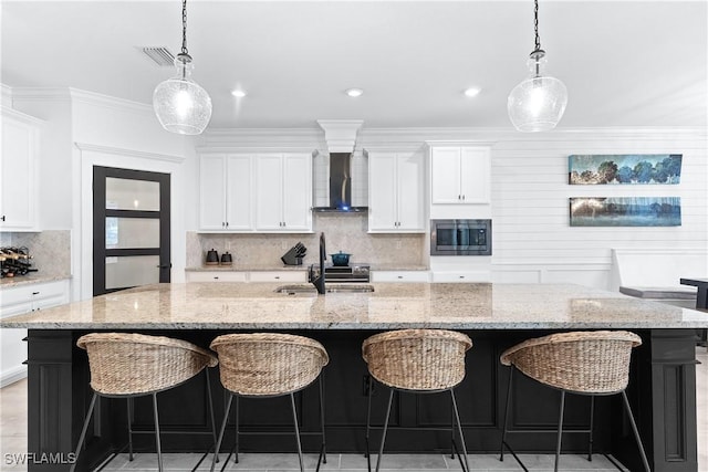 kitchen featuring a sink, a large island, wall chimney exhaust hood, stainless steel microwave, and pendant lighting