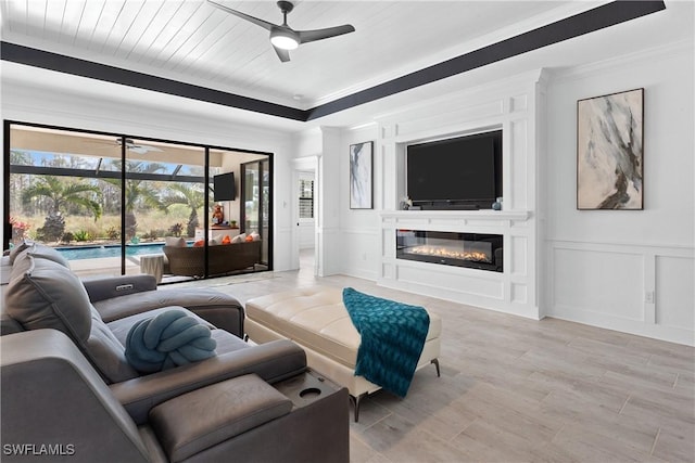 living area with a fireplace, a decorative wall, a ceiling fan, ornamental molding, and wood ceiling