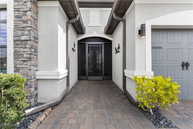 view of exterior entry with a garage, stone siding, and stucco siding