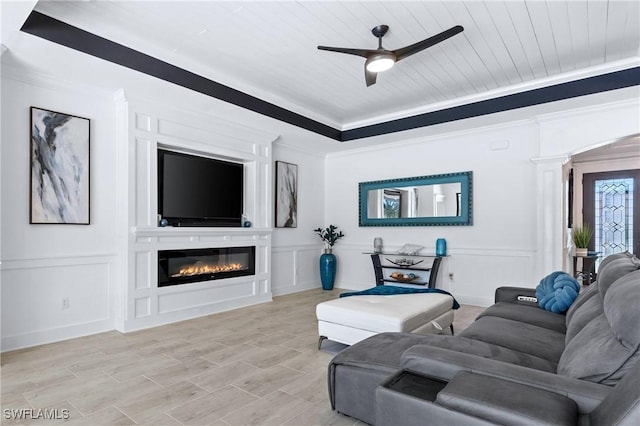 living area featuring a ceiling fan, wood ceiling, crown molding, a fireplace, and a decorative wall