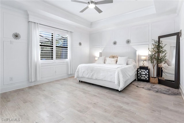 bedroom featuring crown molding, a tray ceiling, a decorative wall, and a ceiling fan