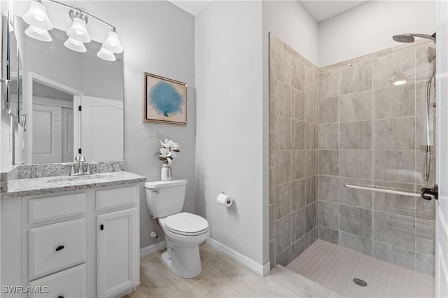 bathroom with toilet, tiled shower, vanity, and baseboards