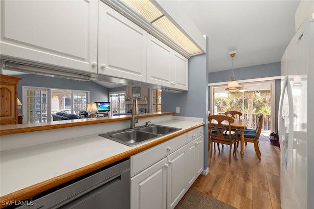 kitchen with stainless steel dishwasher, a sink, freestanding refrigerator, and white cabinets