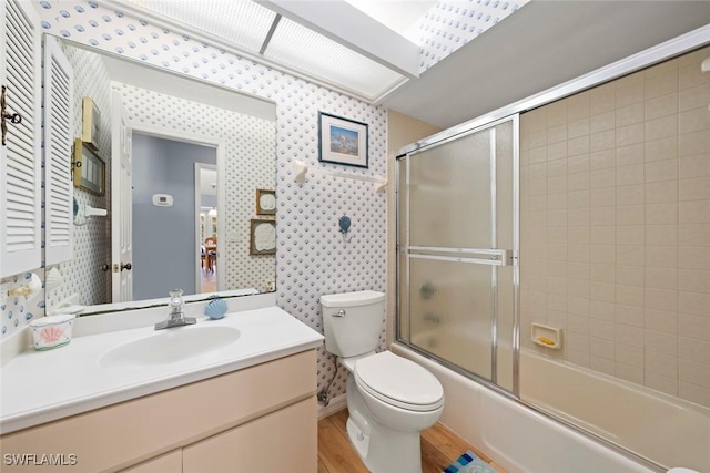 bathroom featuring bath / shower combo with glass door, toilet, vanity, wood finished floors, and wallpapered walls