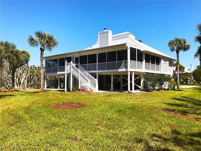 back of property with a sunroom, a lawn, and a chimney