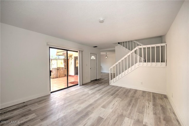 spare room with stairs, a textured ceiling, wood finished floors, and baseboards